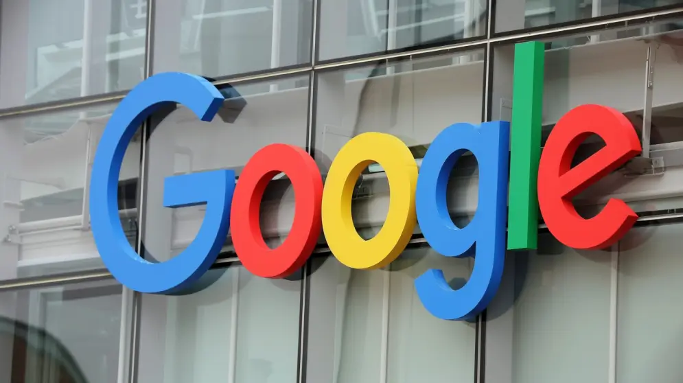 Bilden visar Googles logotyp med stora, färgglada bokstäver på en byggnadsfasad. Glasfönstren reflekterar himlen och skapar ett modernt och elegant utseende, som påminner om dess strävan att rankas högre i sökresultaten.